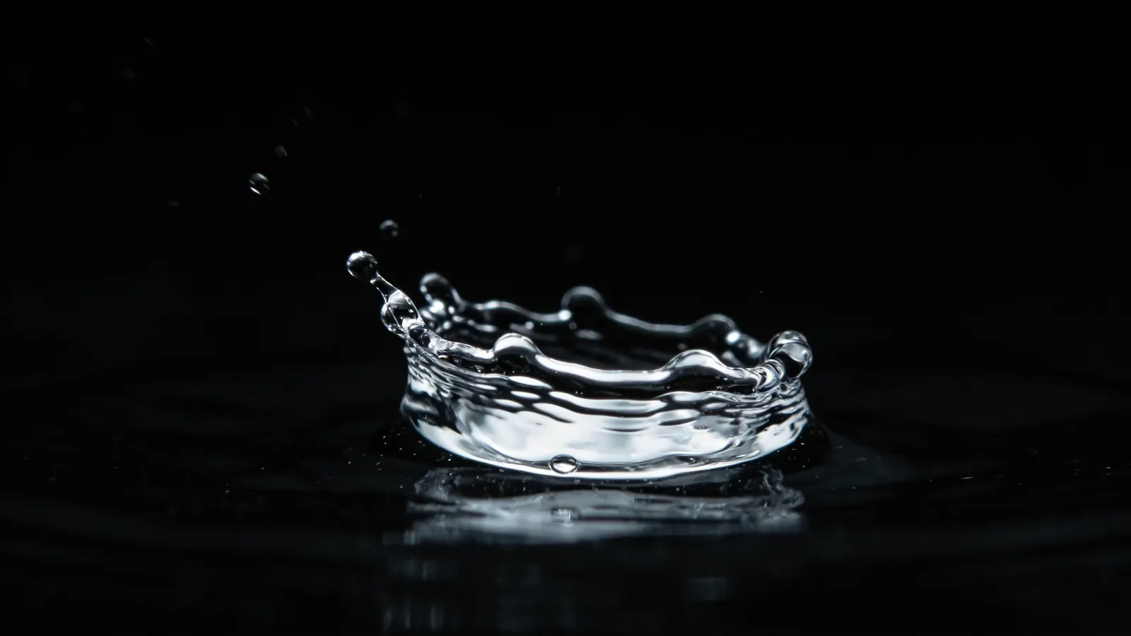 A crown of clean water thrown up by a single droplet, lit fresh green against near-black.