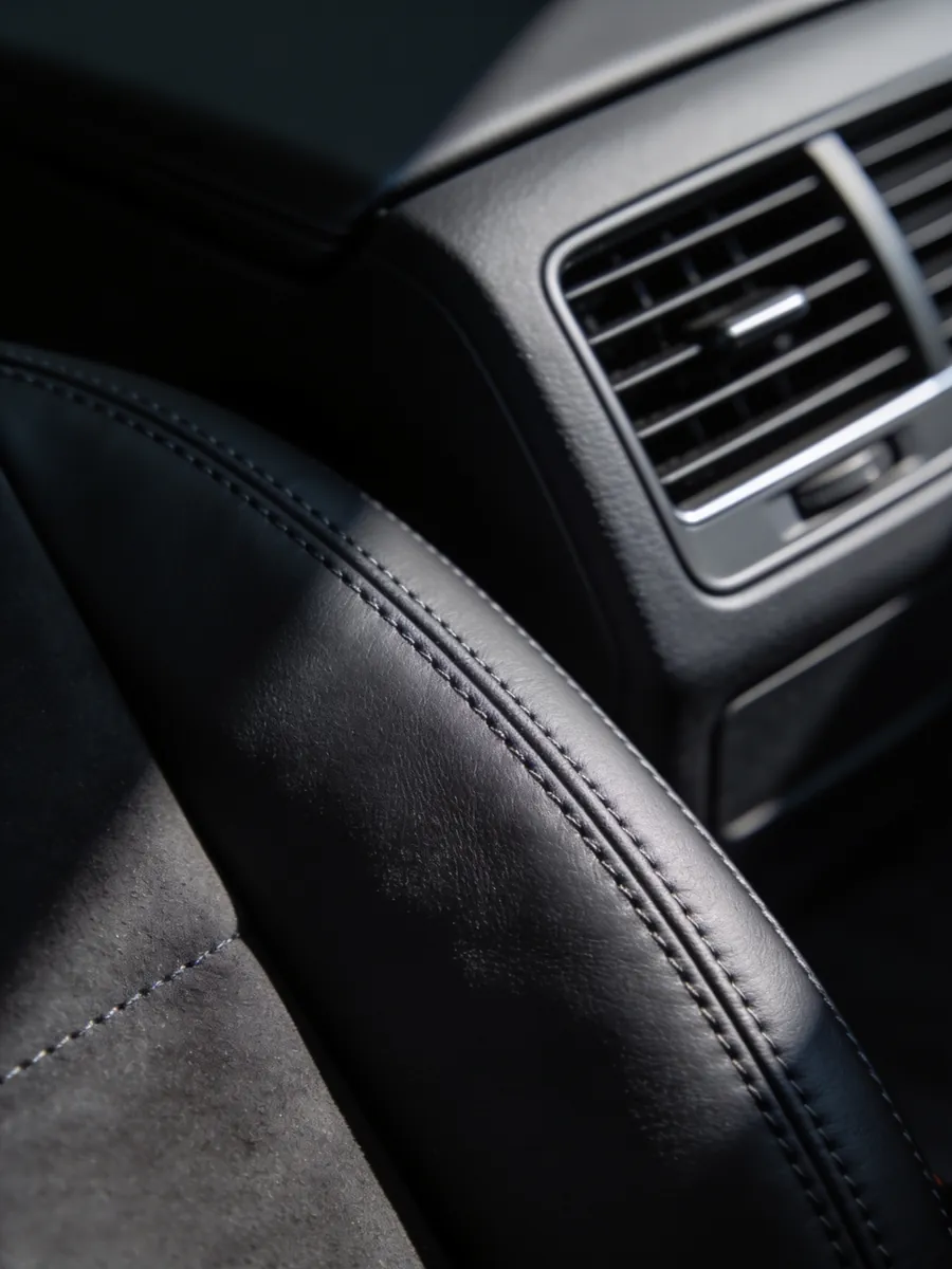 Clean car interior detail — stitched leather beside a dashboard air vent.
